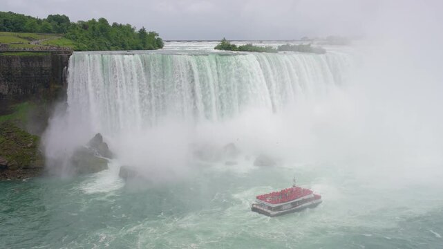 A red tour boat filled with passengers approaches the base of Horseshoe Falls through rising mist in slow motion, Slow Motion