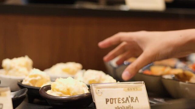 Person Picking Up Potato Salad Bowl at Japanese Buffet Restaurant