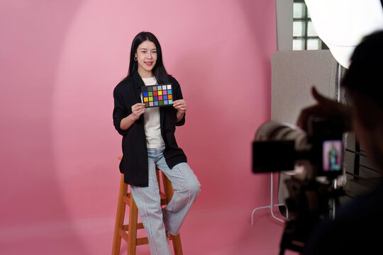 Asian woman holding color checker card during photo studio shoot