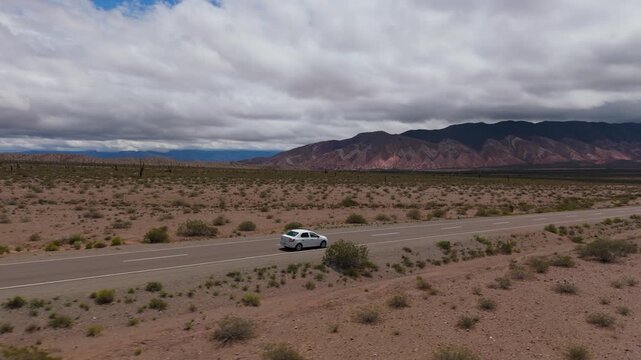 Drone following white car across Recta del Tin Tin desert highway in Salta, aerial angled rearview