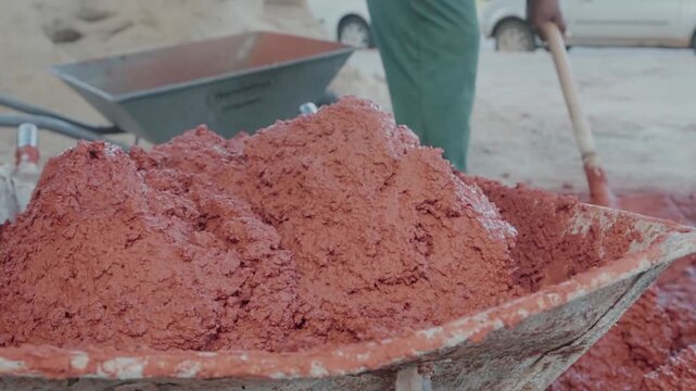 Close up shot of a construction worker preparing a natural building material. A traditional mixture of clay, sand, and straw in a wheelbarrow