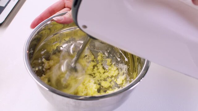 Cooking pastry. Mixing process. Chef hand stirring yellow butter dough in stainless steel bowl with electric mixer beater on table.