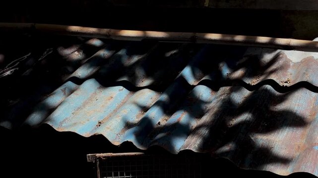 Rustic corrugated metal roof texture with dappled sunlight and deep shadows, showing weathered blue paint and rust