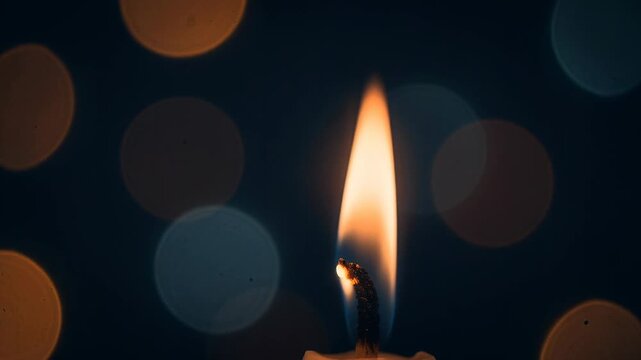 Close up of a burning candle flame with soft bokeh lights in dark background for cozy ambiance