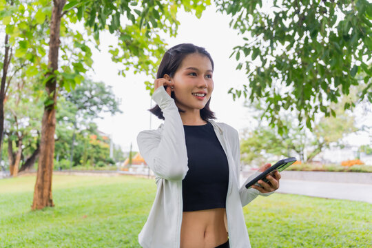 Asian sporty woman using earphone listen to music on smartphone in public park