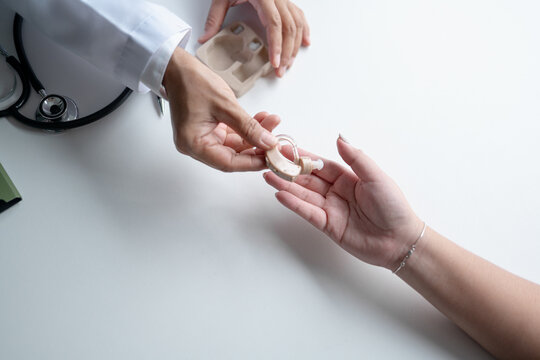 Doctor handing hearing aid to Asian female patient during hearing care consultation at medical clinic