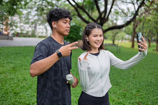 Multicultural Gen Z friends Asian Gen Z woman and African American mixed race man using smartphone taking selfie in green urban park for wellness lifestyle