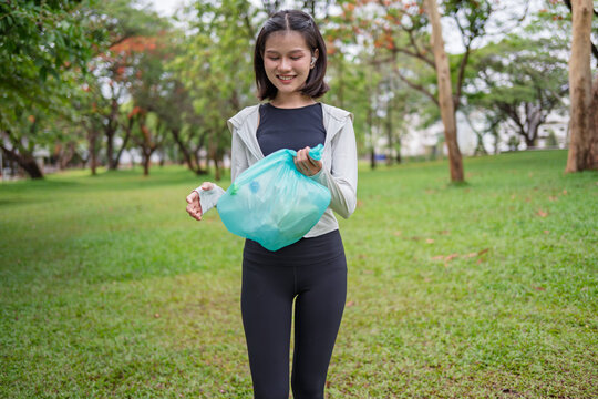 Asian Gen Z woman plogging and collecting trash in green urban park for representing sustainability wellness and positive active lifestyle