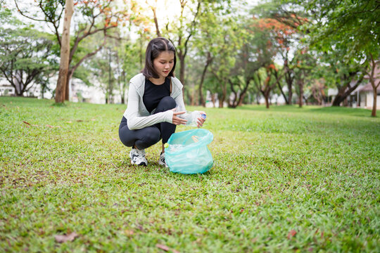 Asian Gen Z woman plogging and collecting trash in green urban park for representing sustainability wellness and positive active lifestyle