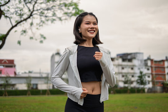 Asian Gen Z woman jogging in green urban park for wellness fitness and active city lifestyle
