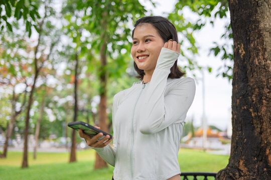 Asian woman with wireless earbuds warming up before jogging in green urban park for wellness lifestyle