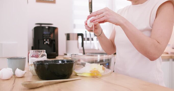Confectioner workflow. Cooking food. Female chef hand braking raw eggs in bowl with butter sugar ingredient making dough home dessert.