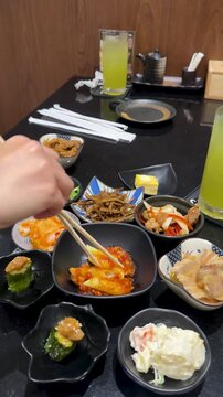 Person Using Chopsticks to Eat Korean Tteokbokki and Side Dishes