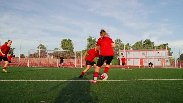 Womens soccer players in red jerseys practice passing, dribbling, and shooting drills on an outdoor artificial turf field during a competitive team training session