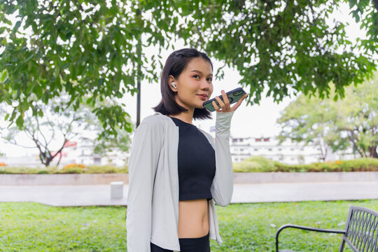 Asian sporty woman open speakerphone talking with friend on smartphone in public park