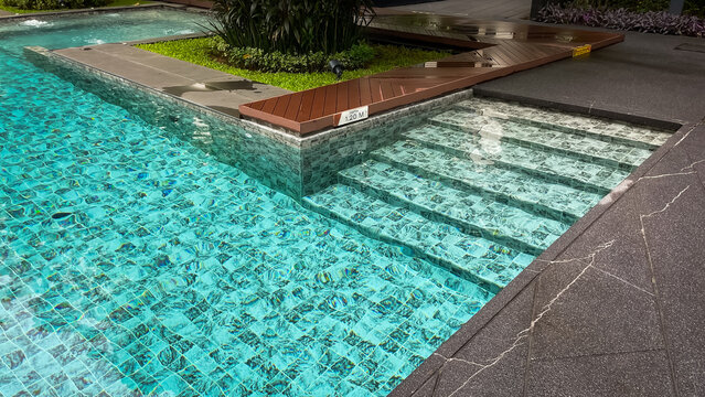 Tiled steps lead to a gently sloping entryway into the outdoor pool of a modern condominium in Thailand.