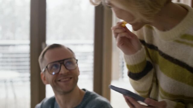 Caucasian adult man slicing oranges on board while woman takes slice, eats, and laughs. Footage is perfect for healthy lifestyle and home cooking advertisements