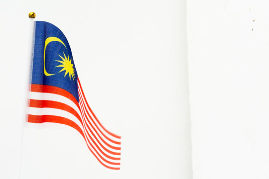 A vibrant Malaysian national flag (Jalur Gemilang) waving gracefully against a clean white wall with ample copy space.