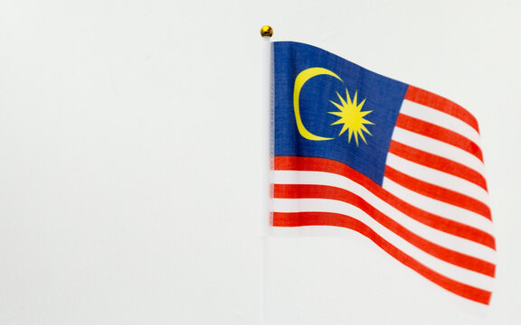 A vibrant Malaysian national flag (Jalur Gemilang) waving gracefully against a clean white wall with ample copy space.