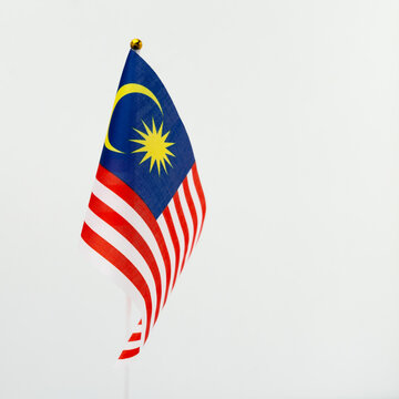 A vibrant Malaysian national flag (Jalur Gemilang) waving gracefully against a clean white wall with ample copy space.