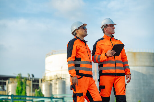 Industrial engineers surveying refinery equipment while holding a digital tablet during a routine facility inspection. Engineering assessment, operational planning, industrial energy infrastructure.