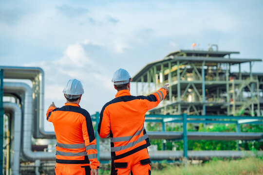 Rear view of industrial engineers inspecting refinery equipment during a routine site assessment. Engineering teamwork, process monitoring, plant operations, maintenance planning, industrial safety.