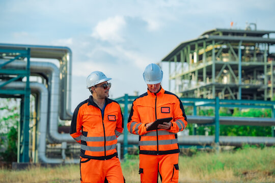 Industrial engineers walking through a refinery while reviewing inspection information digital tablet. Engineering, preventive maintenance, inspection, operational efficiency, industrial safety.