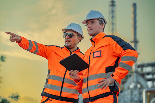 Senior engineer pointing toward refinery equipment while discussing inspection priorities. Engineering leadership, facility assessment, maintenance strategy, industrial safety, energy production.