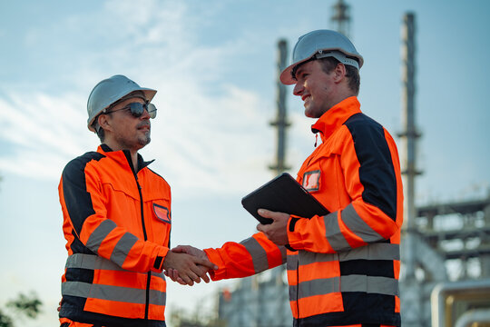 Industrial engineers shaking hands after confirming project progress at a refinery. Successful collaboration, engineering partnership, plant operations, maintenance management, workplace safety.