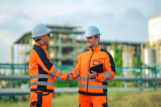 Industrial engineers discussing maintenance procedures beside refinery facilities. Technical consultation, engineering teamwork, digital inspection, industrial operations, energy infrastructure.