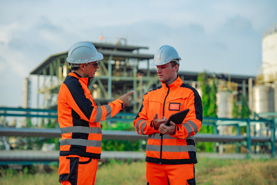 Senior engineer providing site instructions while junior engineer listens digital tablet. Technical mentoring, engineering supervision, industrial communication, refinery inspection 