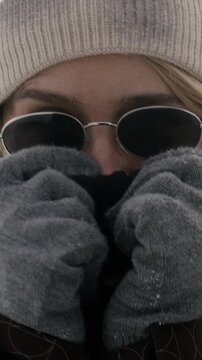 Portrait of Caucasian adult woman wearing sunglasses and beanie, holding collar to stay warm in cold weather. Footage perfect for winter fashion brands and travel promotions, vertical