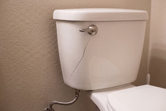 Cracked white toilet tank leaking water in a bathroom