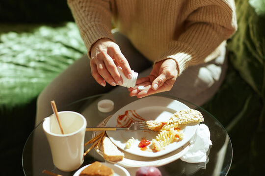 A person holds a white pill bottle and a tablet at a table with leftover food, suggesting a routine of weight management or digestive support after a meal.