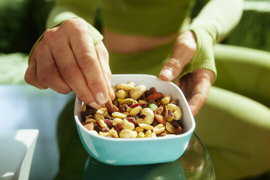 A close-up shot of a woman in athletic wear holding a bowl of trail mix containing nuts, seeds, and dried fruit for a healthy energy boost.