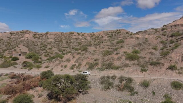 Drone tracking white car along remote road in Quebrada de las Flechas desert, aerial follow left