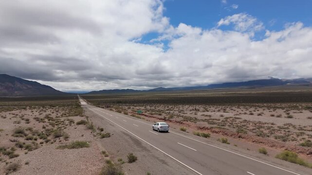 Rear drone orbit of car driving along endless Recta del Tin Tin highway, aerial