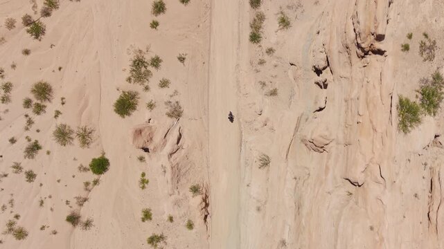 Top down drone of motorcycle riding between sandstone cliffs in Quebrada de las Flechas, aerial backdrop along cliff edge