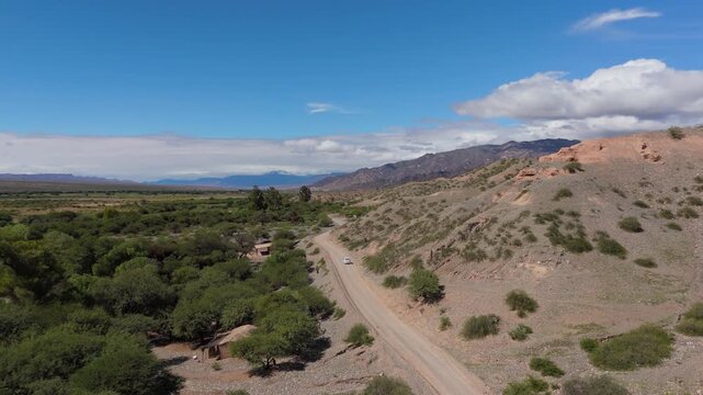 Drone static of single car leaving on dirt road beside green valley near Quebrada de las Flechas, Salta, aerial