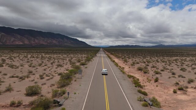 Drone following white car along Recta del Tin Tin under dramatic clouds, aerial dolly forward