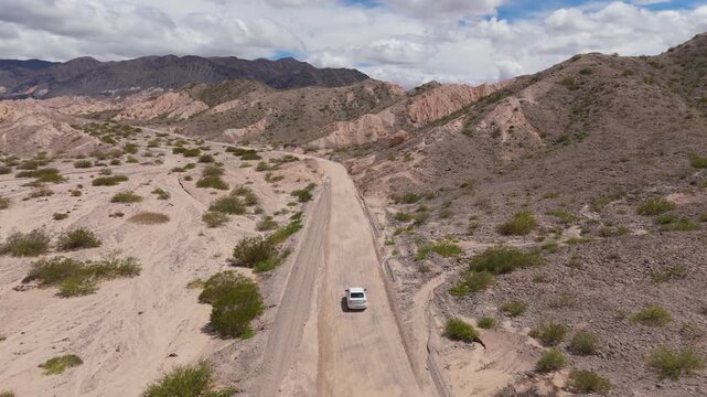 Drone following white SUV on dirt road through Quebrada de las Flechas rock formations, aerial rearview follow