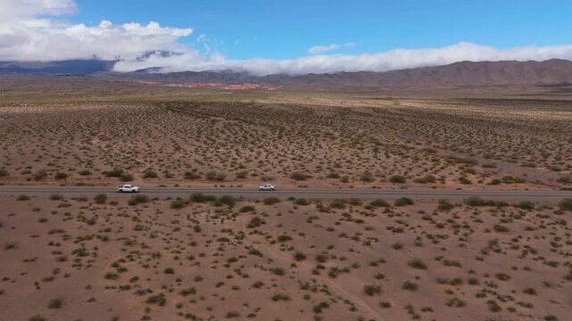 Drone panorama of arid plain surrounding Recta del Tin Tin in Salta, aerial tracking left as traffic crosses in both directions