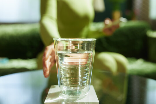 Close-up of a person in lime green sportswear reaching for a glass of water on a white coaster, representing the small, daily habits that contribute to overall fitness and health.