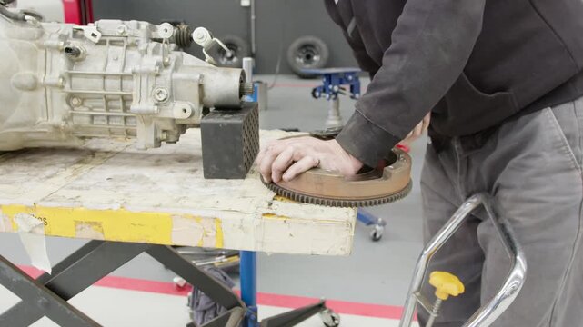 Close-up of a mechanic inspecting and working on a flywheel at a workshop bench. Precision automotive repair and maintenance using professional tools in an industrial setting.