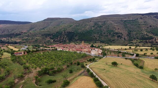 Mirambel ancient medieval village nestled in green hills of Aragon, Spain, surrounded by orchards, farmland and winding roads under a cloudy sky