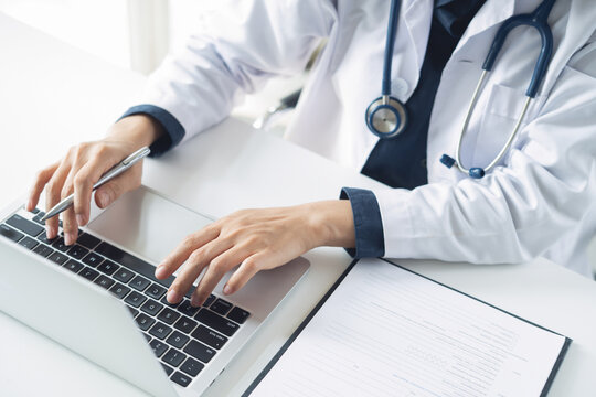 Close up, doctor working on laptop at hospital office with medical document on white desk, searching patient information, medical record at clinic