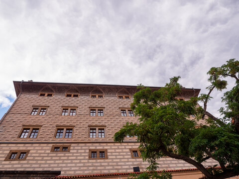 Renaissance Schwarzenberg Palace with distinctive sgraffito facade and a green tree under a cloudy sky near Prague Castle in Prague, Czechia.