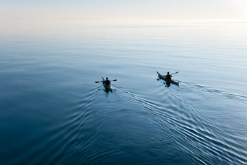 Fototapeta premium Kayakers Paddling Across Calm Waters of Puget Sound at Dawn with Smooth Reflections on Serene Surface
