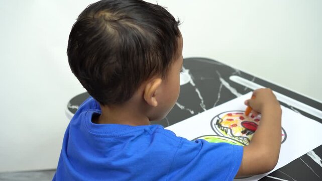 A little Asian boy is focusing on coloring a picture of a donut with crayons, to test the child's creativity, imagination and development.