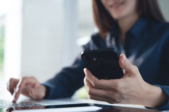 Asian business woman using smartphone and working on laptop computer with digital tablet on office table. 